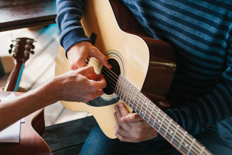 Hands playing an acoustic guitar during a lesson